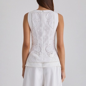 Model wearing House of CB white sleeveless top, rear view, featuring intricate lace and embroidery detail with structured peplum hem