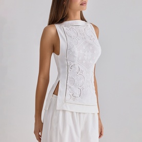 Model wearing House of CB white sleeveless top with floral lace panel detail, styled with matching wide-leg trousers
