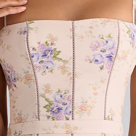 Model wearing cream floral corset top with purple and blue flower print, decorative stitched seam detailing, and thin shoulder straps