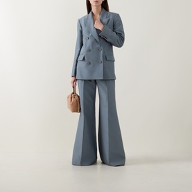 Model wearing slate blue double-breasted blazer and wide-leg flared trousers, styled with a tan mini bag