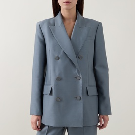 Model wearing a slate blue double-breasted blazer with notch lapels and flap pockets, styled with a white top underneath.