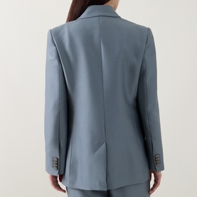 Model wearing a slate blue tailored blazer, back view, with matching trousers, featuring structured shoulders and button cuffs.