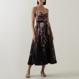 Model wearing Zimmermann Black Floral linen-silk midi dress with corset bodice and full skirt, styled with gold chain belt and nude heels.