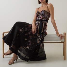 Model wearing Zimmermann Black Floral linen-silk dress with spaghetti straps and lace trim hem, seated, styled with gold strappy sandals.
