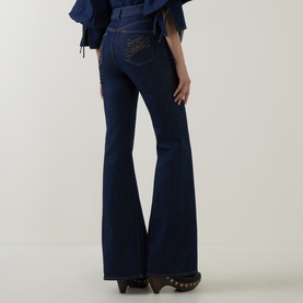 Model wearing Zimmermann Harbour Blue flare jeans, rear view showing embroidered back pocket detail, styled with brown clogs and blue ruffled top