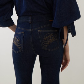 Model wearing Zimmermann Harbour Blue flare jeans, rear view showing gold embroidered pocket detail, styled with matching blue top.