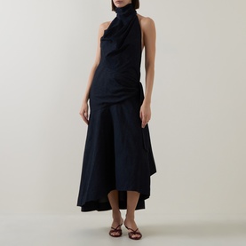 Model wearing Zimmermann Night Sky dress in navy cotton, featuring halterneck, draped bodice and asymmetric hem, styled with brown strappy sandals