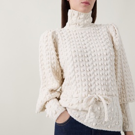 Model wearing Zimmermann Bubble Textured Turtleneck Sweater in cream with puff shoulders, blouson sleeves, front tie, and bubble-knit finish. Styled
