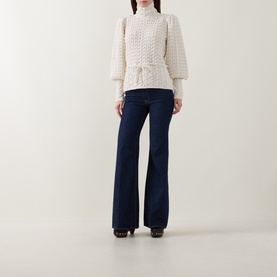 Model wearing Zimmermann Bubble Textured Turtleneck Sweater in cream with puff sleeves and front tie, styled with dark navy flare jeans