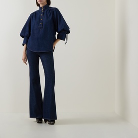 Model wearing Zimmermann Harbour Blue cotton shirt with puffed sleeves and tie cuffs, styled with dark flared jeans and black heels