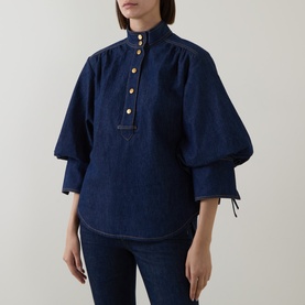 Model wearing Zimmermann Harbour Blue denim shirt with puffed sleeves, gold buttons, and tie cuffs, styled with matching denim trousers.