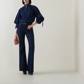 Model wearing Zimmermann Harbour Blue cotton shirt with billowing sleeves and tie cuffs, styled with dark flared jeans and mini bag