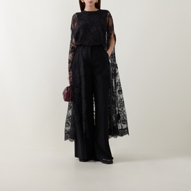 Model wearing Zimmermann Valiant Lace Caped Blouse in black with scalloped lace cape, styled with wide-leg black trousers and burgundy clutch bag.