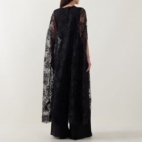 Model wearing Zimmermann Valiant Lace Caped Blouse in black, with long flowing lace cape sleeves and scalloped trim, styled with black wide-leg