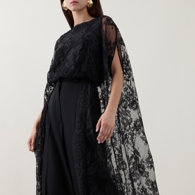 Model wearing Zimmermann Valiant Lace Caped Blouse in black with scalloped lace cape sleeves, paired with wide-leg black trousers.