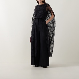 Model wearing Zimmermann Valiant Lace Caped Blouse in black with scalloped lace cape sleeves, styled with wide-leg black trousers.