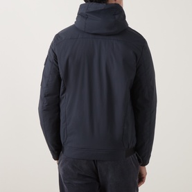 Model wearing Bugatti Quilted Hooded Jacket in blue, rear view showing adjustable toggle hood, sleeve flap pocket with logo patch, styled with