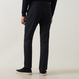 Model wearing navy slim-fit trousers, shown from behind, styled with a navy knit and blue suede trainers