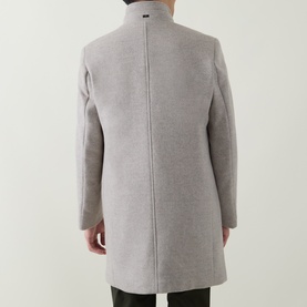 Model wearing Bugatti Logo Longline Coat in stone, rear view showing stand-up collar, centre back seam and rear logo plaque.