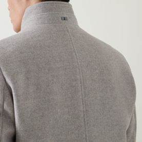 Model wearing Bugatti Logo Longline Coat in stone, rear view showing stand-up collar, rear logo plaque, and soft wool-blend finish.