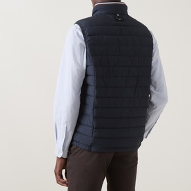 Model wearing Bugatti Air Series Padded Gilet in navy, quilted sleeveless design with funnel neck, styled with light blue shirt and brown trousers.