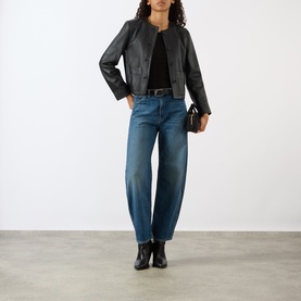 Model wearing Nili Lotan Ophelie Cropped Leather Jacket in black, collarless, styled with blue jeans, black top and ankle boots