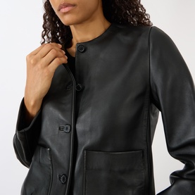 Model wearing Nili Lotan Ophelie Cropped Leather Jacket in black, collarless with front button fastening and patch pocket detail visible.