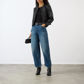 Model wearing Nili Lotan Ophelie Cropped Black Leather Jacket with blue jeans, black top, belt, and ankle boots, carrying small black bag