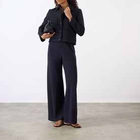 Model wearing Nili Lotan midnight navy cropped jacket with wide-leg trousers and flat sandals, carrying a small black bag.