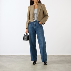 Model wearing Nili Lotan Glen Tan cropped blazer jacket, styled with wide-leg blue jeans, grey top, and carrying a small black handbag.