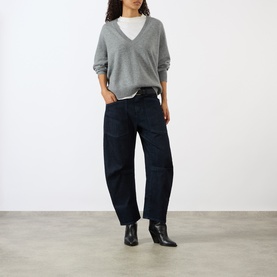 Model wearing Nili Lotan pebble grey heather V-neck knit sweater, styled with dark indigo barrel-leg jeans and black heeled ankle boots.