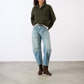 Model wearing Nili Lotan Renata Turtleneck Sweater in Dark Pine Melange, styled with light wash barrel-leg jeans and brown ankle boots.