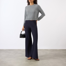 Model wearing Nili Lotan pebble grey heather cropped knit jumper, styled with navy wide-leg trousers and a small black handbag.
