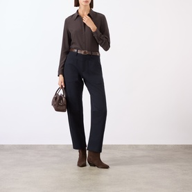Model wearing Nili Lotan chocolate brown silk shirt, styled with dark trousers, brown belt, ankle boots, and small brown handbag.