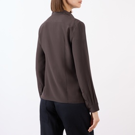 Model wearing Nili Lotan chocolate brown silk shirt, rear view, with navy trousers. Long sleeves, relaxed fit, mock neck collar.