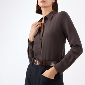 Model wearing Nili Lotan chocolate brown silk shirt with collar and button placket, styled with navy trousers and brown leather belt.
