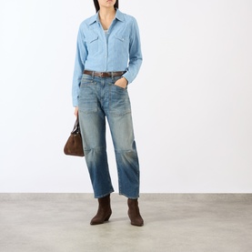 Model wearing Nili Lotan Indigo Chambray cotton shirt with distressed jeans, brown belt, ankle boots, and carrying a brown bag.