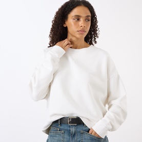 Model wearing Nili Lotan Gladys Sweatshirt in ecru with crew neck and dropped shoulders, styled with blue jeans and black belt