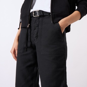 Model wearing Nili Lotan carbon cotton trousers with belt, styled with a black jacket and white top, hand in pocket detail visible.