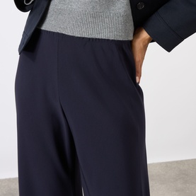 Model wearing Nili Lotan midnight navy wide-leg trousers with elasticated waist, styled with a grey knit and dark blazer.