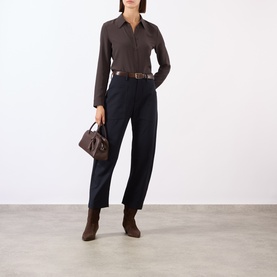 Model wearing Nili Lotan midnight wool trousers, styled with a dark brown shirt, leather belt, ankle boots, and small handbag.