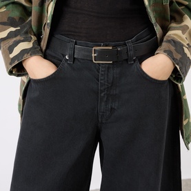 Model wearing black wide-leg jeans with gold-buckle belt, styled with a camouflage jacket. Hands in pockets.