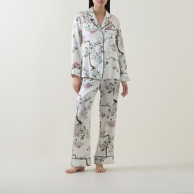 Model wearing Olivia von Halle Lila Ana Blossom Silk Pyjama Set in white with floral bird print, long sleeves and full-length trousers