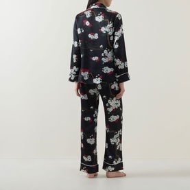 Model wearing Olivia von Halle Lila Ren&eacute; Blossom Pyjama Set in black floral silk, shown from behind, long sleeve shirt and full-length trousers