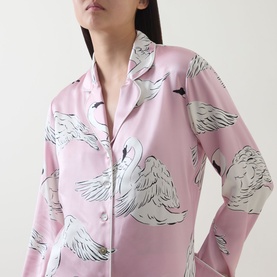 Model wearing Olivia von Halle Lila Selene Swan Pyjama Set in pink silk with white swan print, button-front top with notch collar