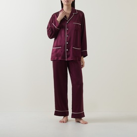 Model wearing Olivia von Halle Yves Silk Pyjama Set in Raisin, long-sleeve button-front top with white piping, matching full-length trousers