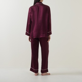 Model wearing Olivia von Halle Yves Silk Pyjama Set in Raisin, rear view showing piped white trim on long-sleeve jacket and full-length trousers
