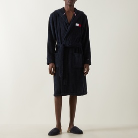 Model wearing Tommy Hilfiger Flag Logo Belted Robe in navy, hooded towelling style with wrap front and belt. Styled with navy slippers