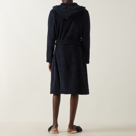 Model wearing Tommy Hilfiger Flag Logo Belted Robe in navy, hooded towelling cotton style with belt, shown from behind with grey slippers