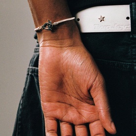 Model with Two Jeys silver bracelet featuring a small charm, styled with a white belt with star detail and dark jeans.